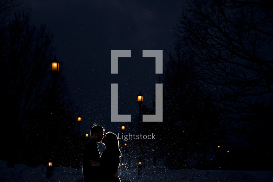 Silhouette of an embracing couple kissing in the snowfall.
