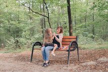 mother and daughter sitting on a park bench 