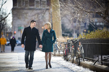 A couple strolling hand-in-hand along a city sidewalk.
