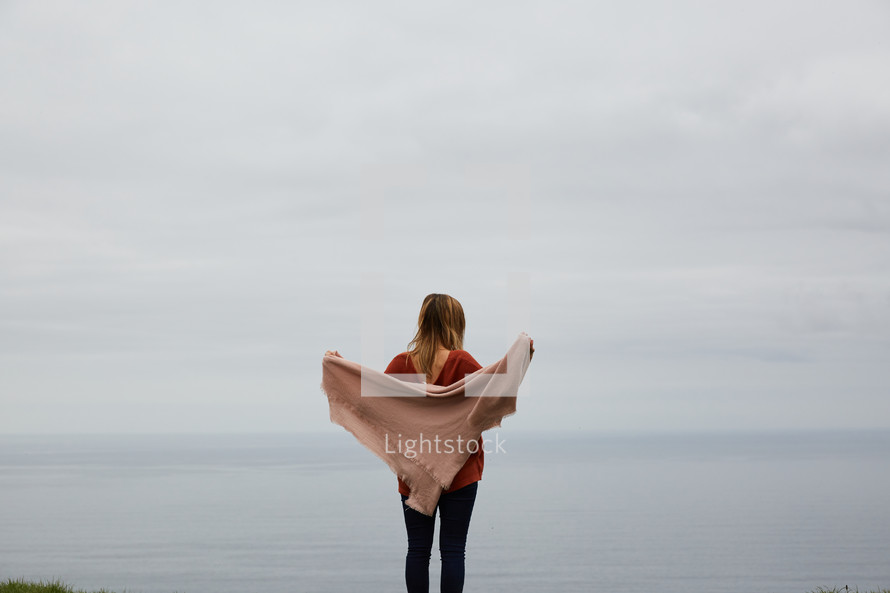 a woman standing at the edge of a cliff taking in the view of the ocean below 
