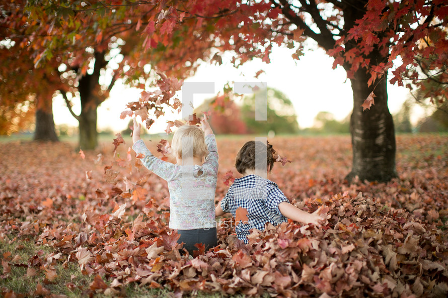 a brother and sister playing in fall leaves 