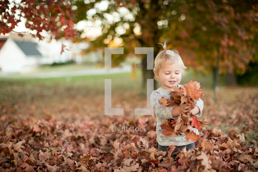 a toddler girl playing in a pile of leaves 