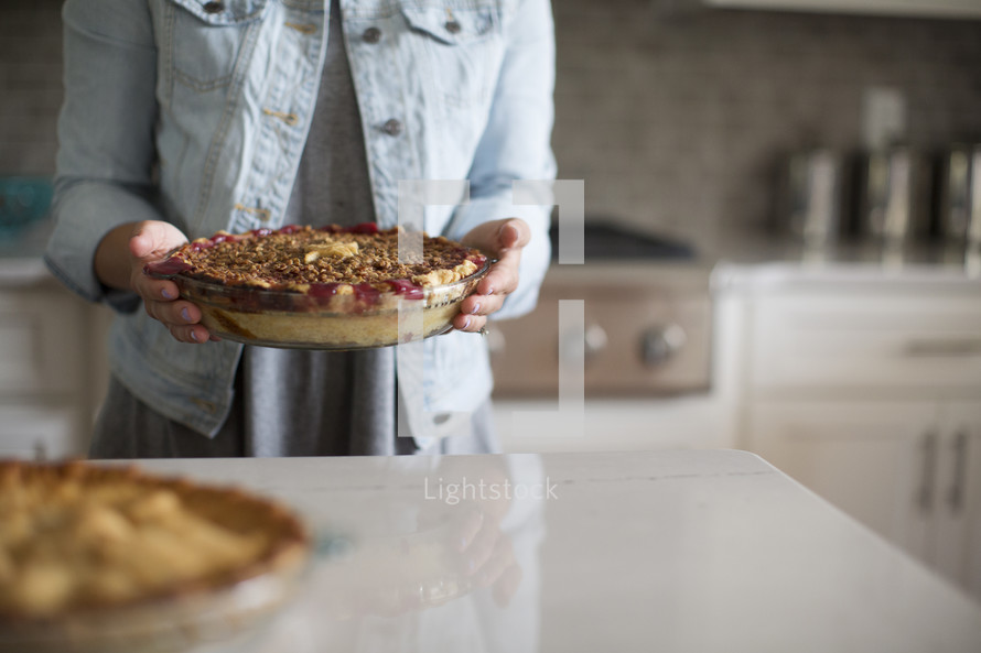 a woman holding a cherry pie in a kitchen.