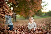a brother and sister playing in fall leaves 