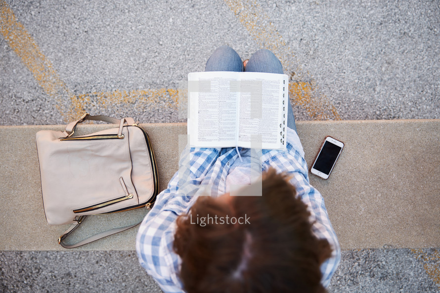 a woman sitting on a stone bench reading a Bible 