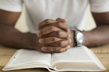 a man with praying hands over the pages of a Bible.
