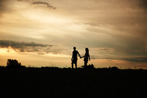 silhouette of a couple walking hands at sunset 