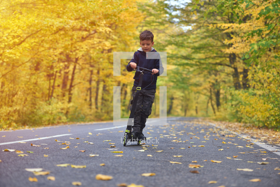 boy riding scooter, outdoors in autumn environment on sunset warm light