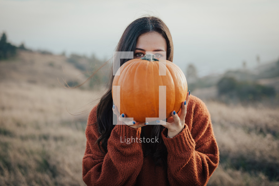 a woman holding up an orange pumpkin 
