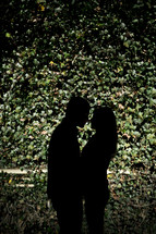 silhouette of a couple about to kiss in front of an ivy covered wall