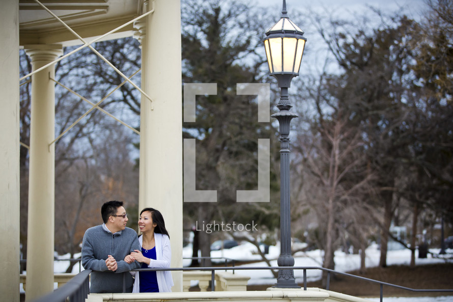 Embracing couple standing outside on a balcony by a lamppost. 
