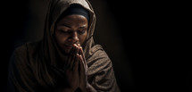 Christian woman in contemplative prayer with hands clasped and eyes closed, serene expression.