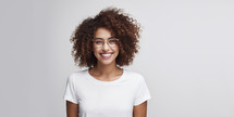 Smiling young woman with curly hair and stylish glasses on a light background.