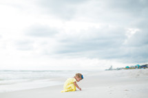 a toddler girl playing in sand on the beach 