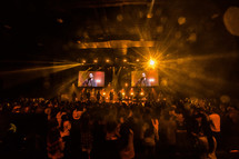 A large audience in front of a stage lit by bright lights.