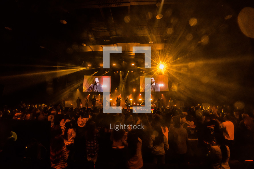 A large audience in front of a stage lit by bright lights.