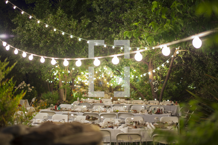 strand of glowing lights over folding chairs at an outdoor wedding