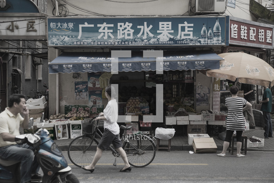 a woman pushing a bicycle through a Chinese market