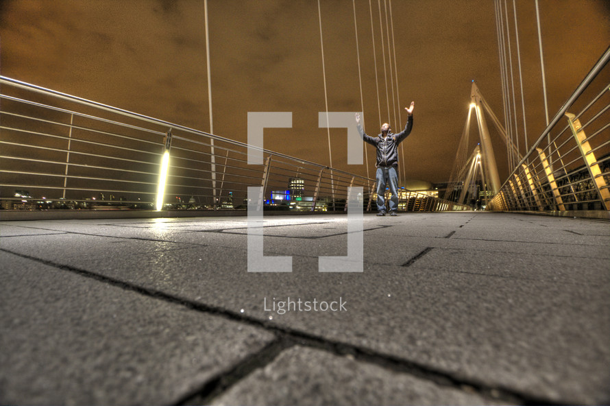Man standing on bridge with arms raised