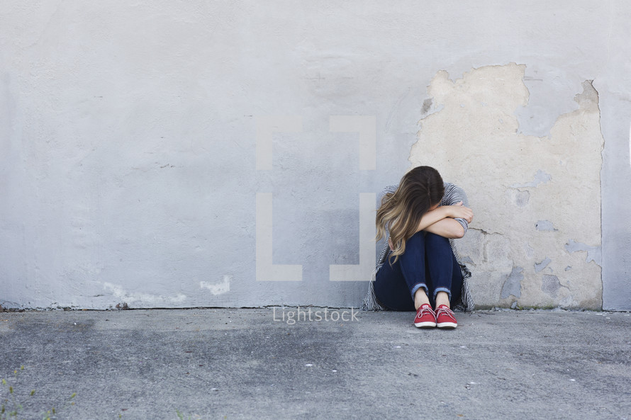 a sad woman crying sitting on a sidewalk 