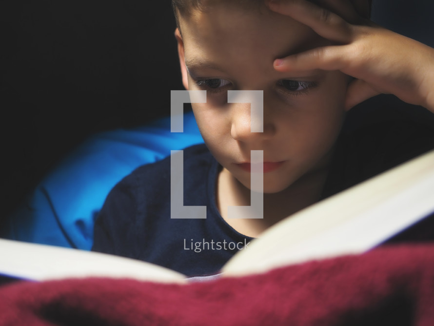 boy reading a book inside at dim spot light