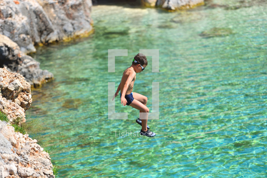 Little boy jumping off cliff into the ocean. Summer fun lifestyle. Brave kid