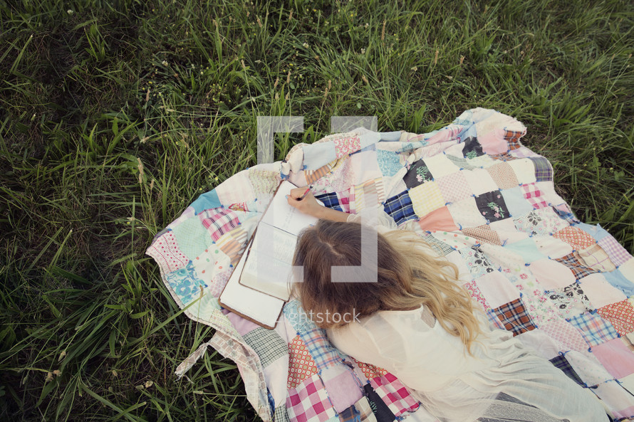 woman sitting outdoors reading a book lying on a blanket 