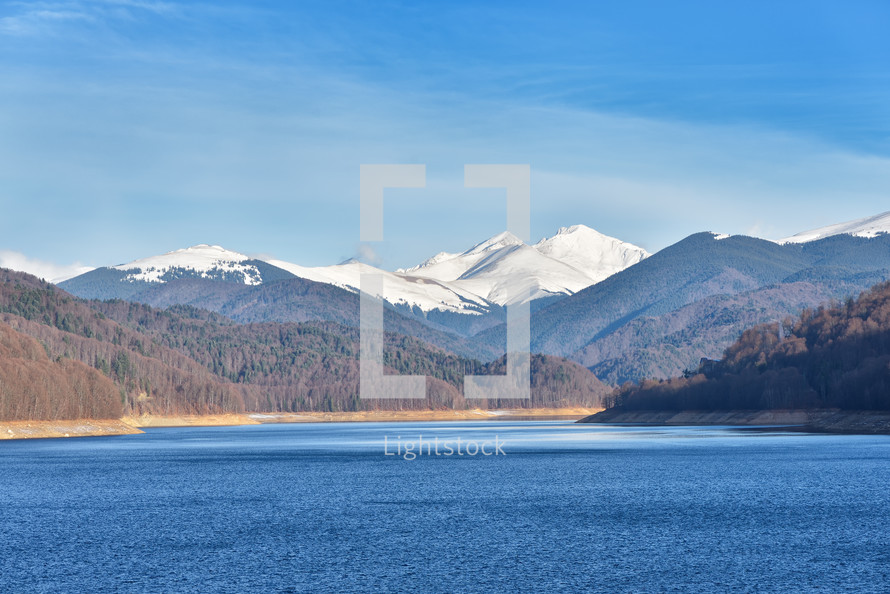 Mountain lake panorama against cloudy sky and mountains covered with snow