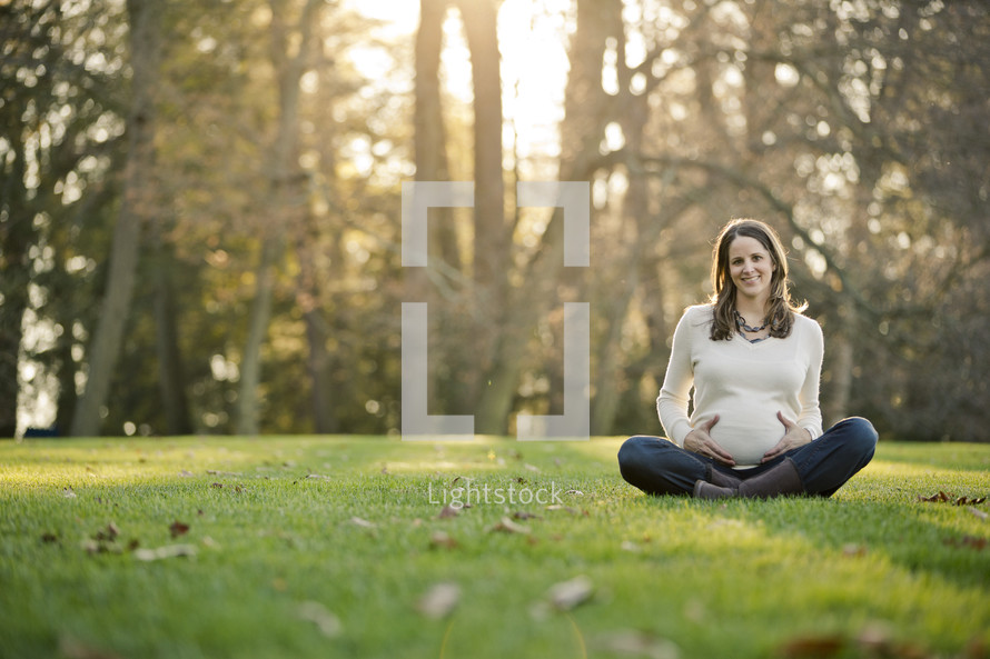woman sitting in the grass with her hands on her pregnant belly