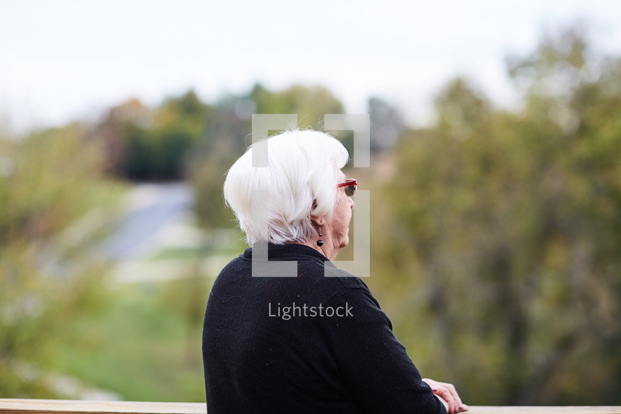 elderly woman looking over a railing thinking 