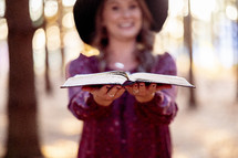A woman standing in the woods with an open Bible 