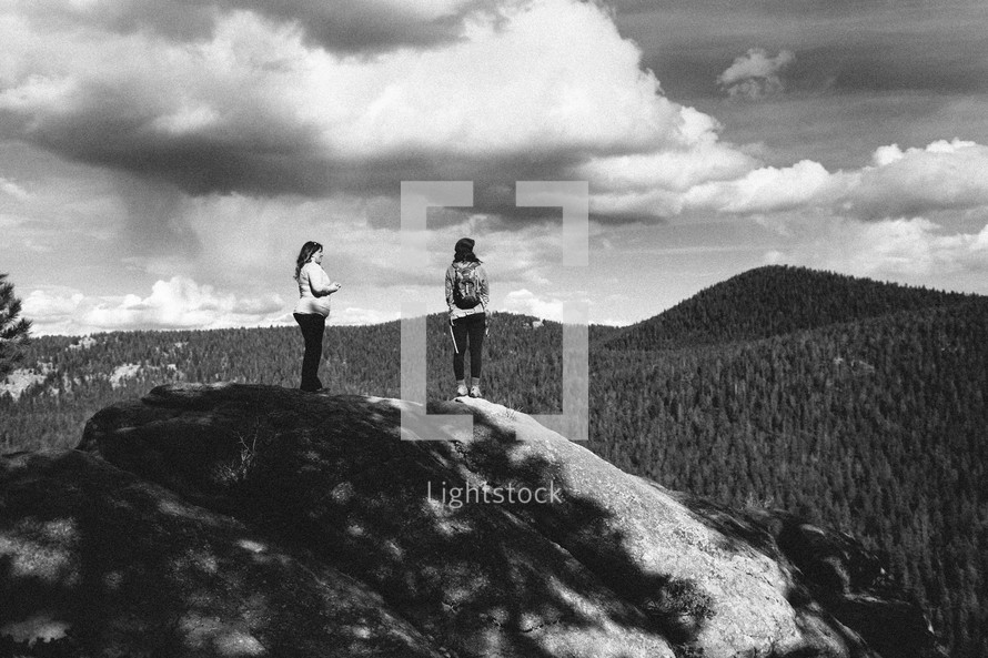 two women stand on top of a rock in the wilderness