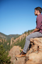 a man siting on a rock looking out at a mountain view 