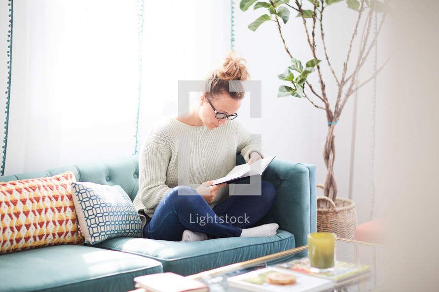 a woman reading a book sitting on a couch 
