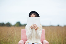 a woman sitting in a chair in a field reading a Bible 