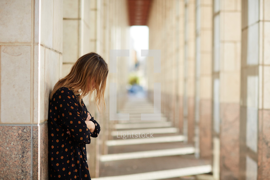 a woman looking down standing alone in a hallway