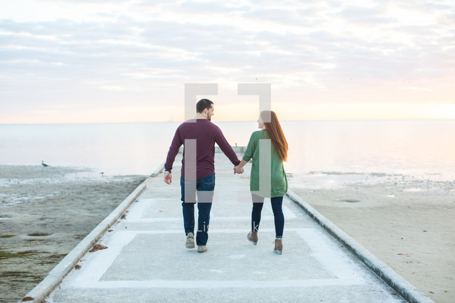 a couple holding hands walking on a beach pier