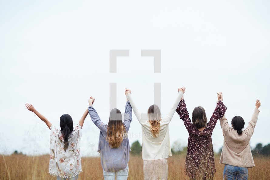 group of women standing a field with raised hands 