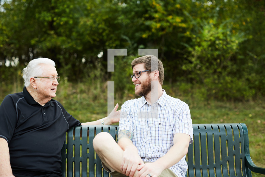 elderly man praying with and talking to a young man 