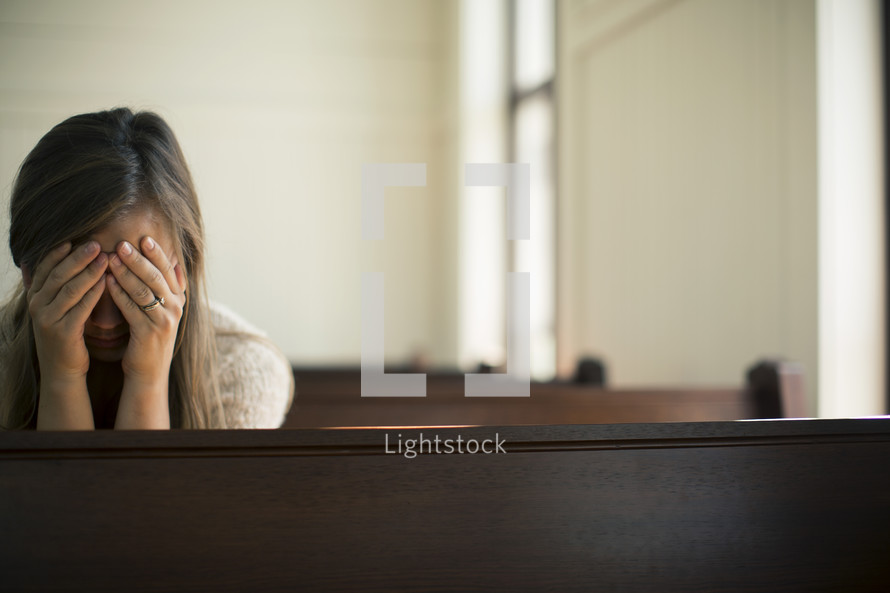 Woman with her face in her hands, praying in a church pew.