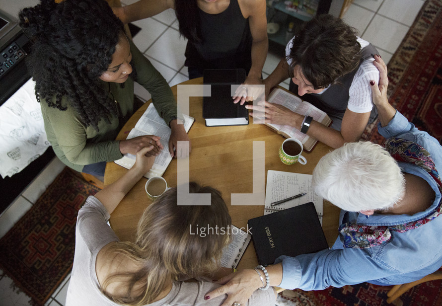 woman's group Bible study holding hands in prayer around a table 