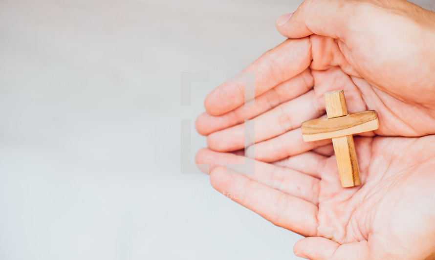 small wooden cross in cupped hands 