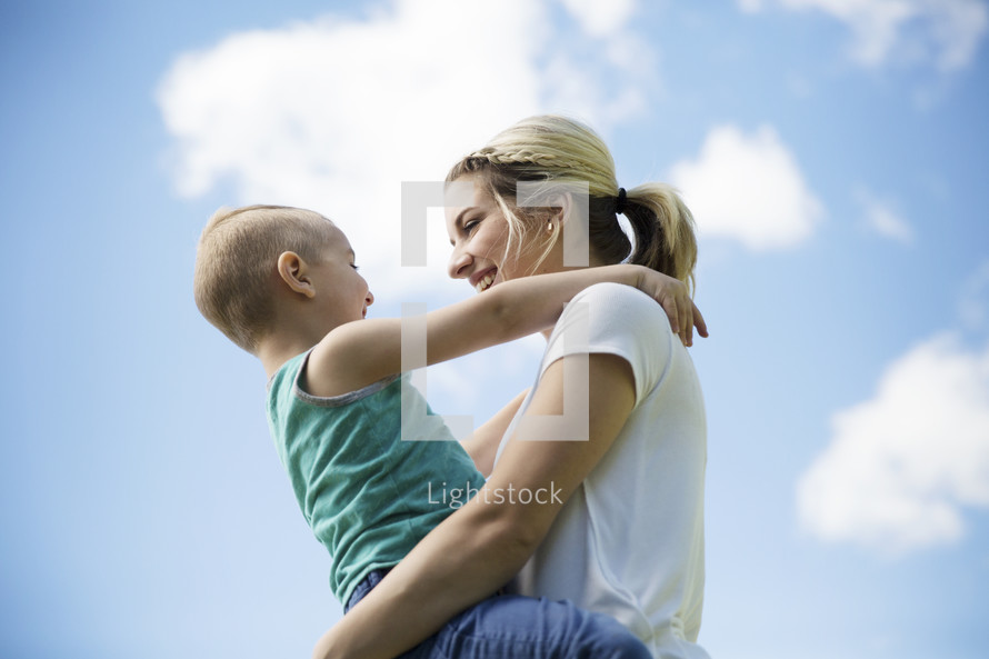 a mother holding her son outside with a blue sky.