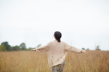 a woman with outstretched arms walking through a field 