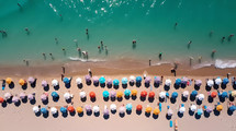 Vertical aerial view of a beach full of colorful umbrellas near the sea in Summer