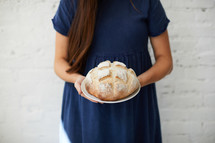 a woman holding a loaf of homemade bread 