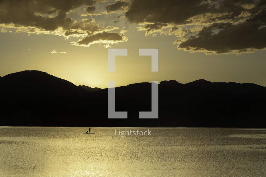 A Silhouette Paddleboarder with their dog on a mountain lake at sunset located in Loveland Colorado