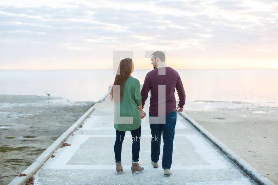 a couple holding hands standing on a beach pier 