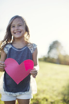 a girl child holding a paper heart 