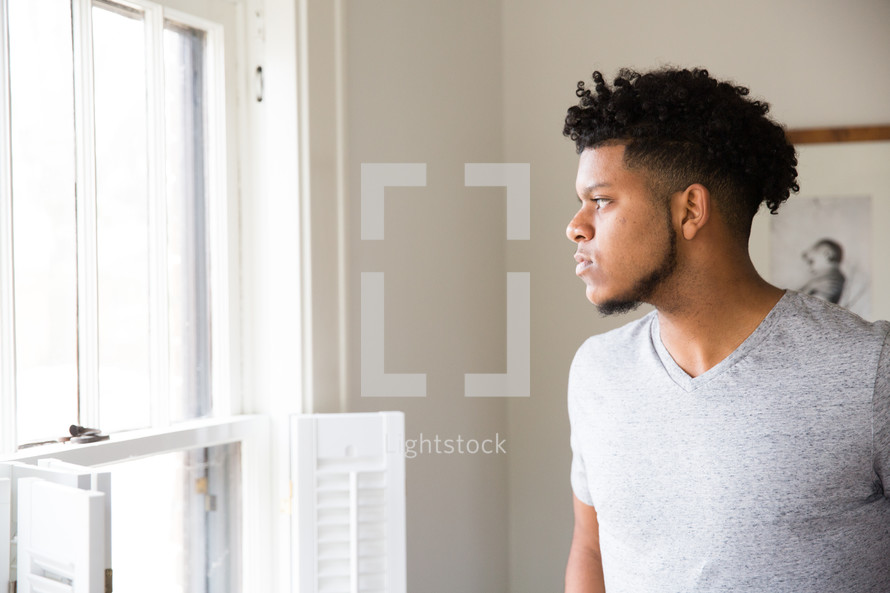 African American young man looking out a window 